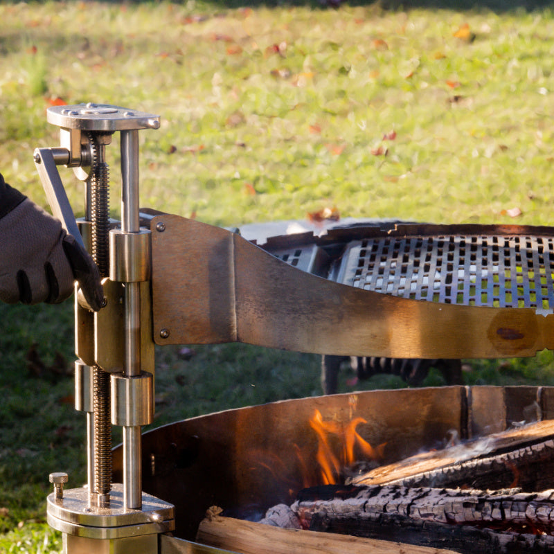 Hand shown operating Control Tower crank to raise and lower the Versa Grate over a live fire in grill.